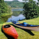 Two kayaks along the grassy shore of a narrow opening in the pond surrounded by trees